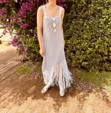 Vestido tejido en lurex color plateado, con diseño geométrico en cuero en el frente y flecos en el ruedo. Breteles finos de cuero con tientos plateados.