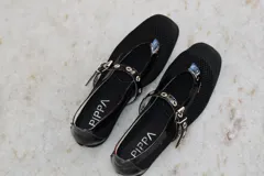 Ballerina Ines de tela negra con detalles de cuero y forrería vacuna. Presenta tira con hebilla ajustable y ojalillos metálicos sobre el empeine.
