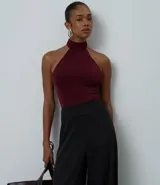 Body de mujer con diseño halter, confeccionado en tejido rib acanalado con acabado brillante. Presenta cuello alto con cierre posterior, corte ajustado al cuerpo y diseño sin mangas.