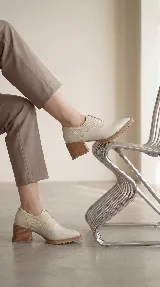 Zapato tipo slip-on color marrón, confeccionado en cuero natural con combinación de texturas lisas y grabadas. Presenta un diseño de punta almendrada, taco cuadrado de madera y suela dentada.