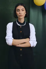 Mono largo de color negro con cierre frontal de botones vintage de distintos colores. Presenta un diseño sin mangas, con bolsillos laterales y una cinta para herramientas en la parte trasera.