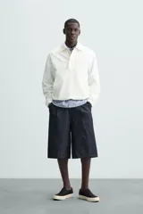 Cazadora tipo canguro de calce relajado, color blanco roto o crema, confeccionada en mezcla de lyocell y algodón. Presenta cuello solapa con cierre frontal de botonadura oculta, manga larga con puños elásticos y bolsillos frontales de vivo. El bajo es ajustable con elástico oculto en los laterales.