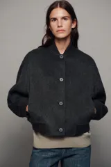 Cazadora bomber beige confeccionada en hilatura con lana, con cuello subido, manga larga y bolsillos frontales. Presenta cierre frontal con botones oscuros y puños, cuello y ruedo en tejido rib.
