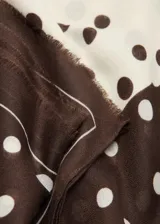 Pañuelo rectangular de tejido fluido con diseño estampado de lunares y terminaciones deshilachadas.