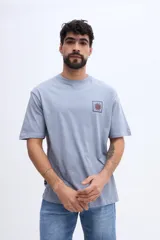 Remera oversize de manga corta color celeste, de corte relajado y amplio, confeccionada en algodón. Presenta un gran estampado en la espalda dividido en cuatro paneles con motivos gráficos (un sol, peces, ondas y formas abstractas) junto con inscripciones de la marca y estilo de vida.