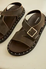 Sandalias negras de cuero con tiras cruzadas y ajuste con hebilla. Decoración de tachas plateadas en la suela.