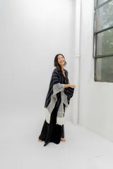 Ruana tejida en tonos azul marino y crudo, con diseño a rayas verticales y detalle de flecos en el ruedo. Presenta un patrón de espiga en los bordes.