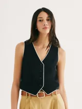 Chaleco negro de tejido liso, con escote en V ribeteado en blanco y cierre frontal de botones oscuros.