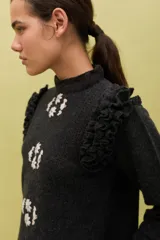 Sweater de lana color celeste, con cuello redondo, mangas largas y volados decorativos en los hombros. Presenta bordados florales artesanales en el frente y detalles de tejido calado vertical.
