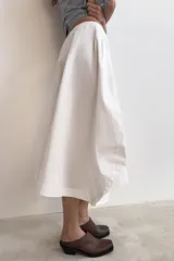 Falda midi de tiro medio en color blanco, con diseño asimétrico en el bajo y bolsillos delanteros. Cuenta con cierre lateral oculto.