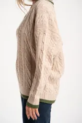 Sweater de lana y nylon color beige jaspeado, con diseño de punto trenzado (cable knit) en todo el cuerpo y mangas. Presenta cuello en V con ribete de dos franjas verdes y puños y bajo con ribete verde liso.