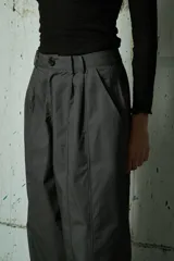Pantalón de corte holgado y tiro alto en color gris oscuro, con pinzas frontales y costuras verticales decorativas a lo largo de las piernas.