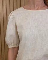 Blusa blanca de lino, con cuello redondo y mangas cortas abullonadas con frunces en los hombros.
