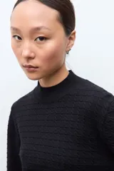 Sweater de punto color crudo con cuello alto tipo media polera, manga larga y diseño con textura de líneas horizontales. Presenta un borde inferior con terminación ondulada.