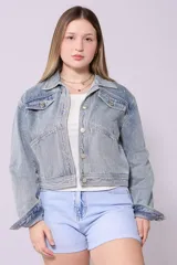 Campera de jean de lavado celeste claro, con diseño clásico de cuello y botones metálicos. Presenta detalles de pequeños brillos o tachas plateadas sobre la tela, especialmente visibles en los bordes de los bolsillos y costuras.