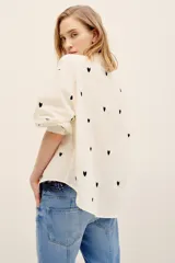 Camisa de algodón color crudo con estampado de corazones negros, de corte holgado, manga larga abullonada y cierre frontal de botones.
