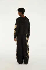 Pantalón de jogging negro de tiro medio, con cintura elastizada y cordón ajustable. Presenta un diseño holgado y estampado botánico localizado en tono claro sobre una de las piernas.