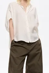 Camisa de manga corta tipo murciélago, color blanco, con cuello camisero y cierre frontal de botones.