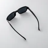 Lentes de sol polarizados con armazón translúcido gris mate y cristales oscuros, de diseño rectangular y detalles metálicos en las patillas.