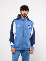 Campera deportiva Umbro del Club Nacional de Football, con cierre frontal, capucha ajustable con cordones y diseño en bloques de color azul, celeste y blanco. Presenta el logo de la marca y el escudo del club bordados en el pecho.