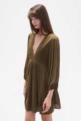 Vestido corto de color verde militar, con escote en V profundo, mangas largas con puños elásticos y detalles de encaje y bordados en el frente. Presenta una falda con vuelo y textura de pequeños puntos en relieve.