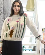 Sweater de punto color blanco crudo, confeccionado en lana merino, con diseño de flores y plantas bordadas y en relieve en tonos rosas y verdes, cuello redondo y mangas largas.
