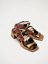 Sandalias de cuero con acabado de charol metalizado en color dorado, con tiras cruzadas en el empeine, taco cuadrado de 4,5 cm y correa ajustable en el tobillo.
