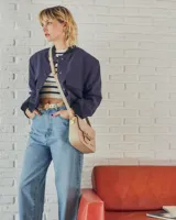 Cartera negra de cuero charolado con solapa y cierre de broche. Presenta un detalle metálico dorado en forma de freno de caballo en la parte frontal y una correa ajustable.