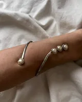 Brazalete rígido plateado con textura martillada y apliques de perlas.