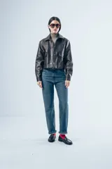 Chaqueta de cuero sintético en color marrón oscuro, con cuello clásico, cierre frontal con botones a presión y dos bolsillos aplicados en el pecho. Presenta un corte recto y estructurado.