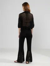 Camisa corta de punto abierto con cuello tipo polo, cierre frontal de botones y mangas tres cuartos. Presenta un diseño calado y un botón decorativo en forma de flor.