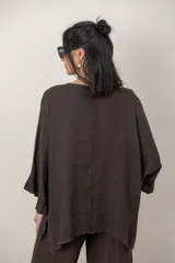 Blusa de lino color verde militar, holgada, de manga 3/4 con volados en los puños, cuello redondo y detalle de alforzas horizontales en el dobladillo.