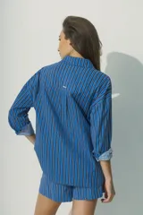 Camisa de corte relajado con diseño de rayas verticales en tonos rojos, marrones y blancos. Presenta cuello clásico, cierre frontal con botones al tono y mangas largas con puños que permiten un estilo arremangado.