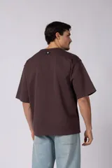 Remera de corte oversize color beige, con cuello redondo y etiqueta decorativa pequeña en el ruedo inferior.