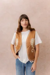 Chaleco corto de efecto gamuza en color tostado, con bordados decorativos en contraste y terminaciones bordadas en los bordes. Presenta escote en V y diseño recto.