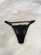 Conjunto de lencería de encaje negro compuesto por un bralette triangular, una tanga y un portaligas integrado. El diseño presenta detalles de encaje floral, breteles regulables y tiras elásticas ajustables.