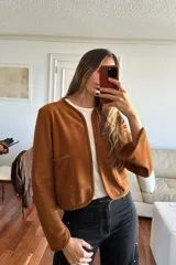 Camisa de gamuza color cognac con cuello redondo, cierre frontal abierto y bolsillos frontales tipo parche. Presenta mangas largas con puños ligeramente acampanados y un corte recto.
