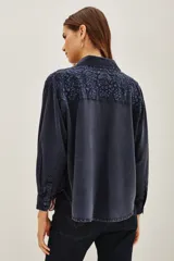 Camisa de corte amplio y holgado, confeccionada en viscosa con efecto lavado. Presenta detalles bordados en los hombros, cuello clásico, cierre frontal con botones y mangas largas con puños.