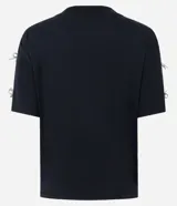 Camiseta blanca de algodón con cuello redondo y mangas cortas, decorada con pequeños lazos brillantes en los laterales de las mangas.
