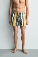 Bañador de hombre con estampado de rayas verticales anchas en tonos amarillo mostaza, azul oscuro desgastado, blanco y gris. Posee cintura elástica con cordón ajustable y bolsillos laterales.