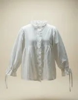 Camisa blanca de algodón con silueta holgada, detalles de tablas hechas a mano en el frente, cartera con botones y volados suaves en el cuello. Cuenta con mangas amplias y puños ajustables.