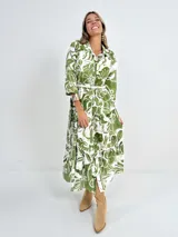 Vestido camisero midi de algodón con estampado floral en tonos verde y blanco. Tiene cuello camisero, mangas 3/4, botones frontales, falda escalonada y cinturón de soga.