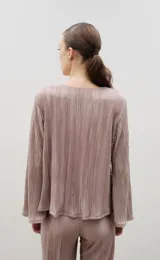 Blusa plisada de color crema con escote en V y mangas largas ligeramente acampanadas. Presenta una textura plisada en toda la prenda que aporta caída y movimiento.