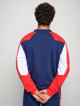 Buzo de felpa con diseño de bloques de color, predominantemente rojo en el cuerpo y azul marino en las mangas y hombros. Presenta el escudo del Club Nacional de Football y el logo de Umbro en el pecho.