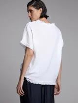Remera blanca de corte holgado con cuello redondo y flecos en las mangas y el ruedo.