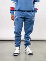 Pantalon de jogging azul de felpa, con franjas laterales en blanco y azul marino. Presenta el escudo del Club Nacional de Football en el muslo derecho y el logo de Umbro en el izquierdo.