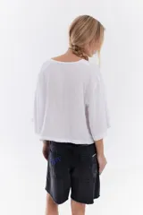 Blusa de lino italiano color beige, de manga corta, con escote en V y cierre frontal mediante lazos o moños.