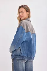 Campera de jean con diseño bicolor, combinando paneles en color gris oscuro y azul denim. Presenta cuello camisero, cierre frontal con botones metálicos y corte holgado.