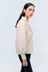 Camisa color crema a rayas verticales con bordado floral en el pecho, cuello mao y mangas largas abullonadas con puños elásticos.