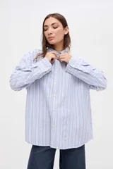 Camisa de corte oversize con diseño de rayas verticales finas en tonos claros. Presenta cuello clásico, cierre frontal con botones y mangas largas con puños abotonados.